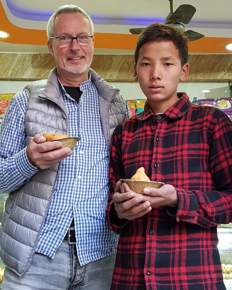 Alain Rouveure standing with a young man in Nepal, both holding food in leaf bowls